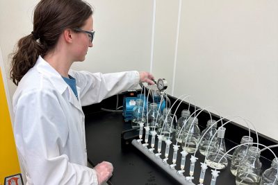 A student in a white lab coat operates equipment in a laboratory